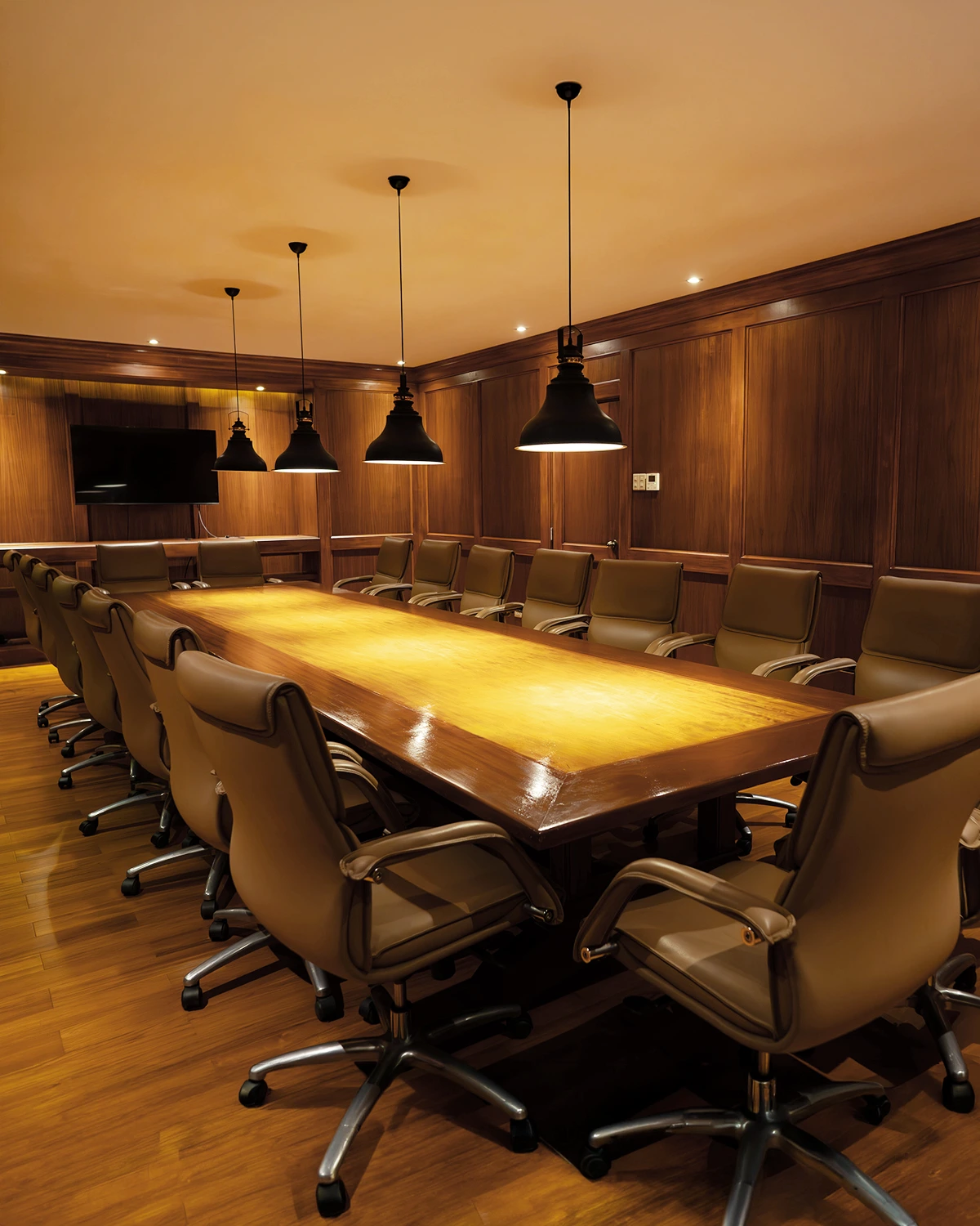 Wood-panelled boardroom with a long conference table, leather chairs, and a wall screen