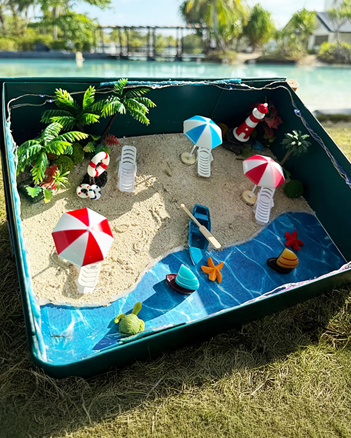 A Design Your Own Resort diorama box - miniature beach, umbrellas and boats - on the grass by the lagoon