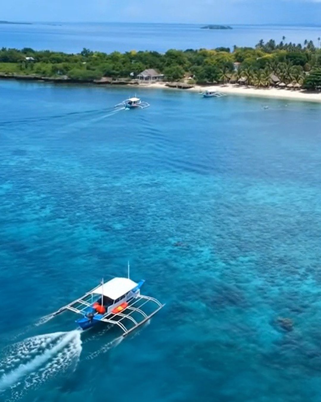 The Miss Flirt outrigger on an island-hopping run, guests dangling feet over the water