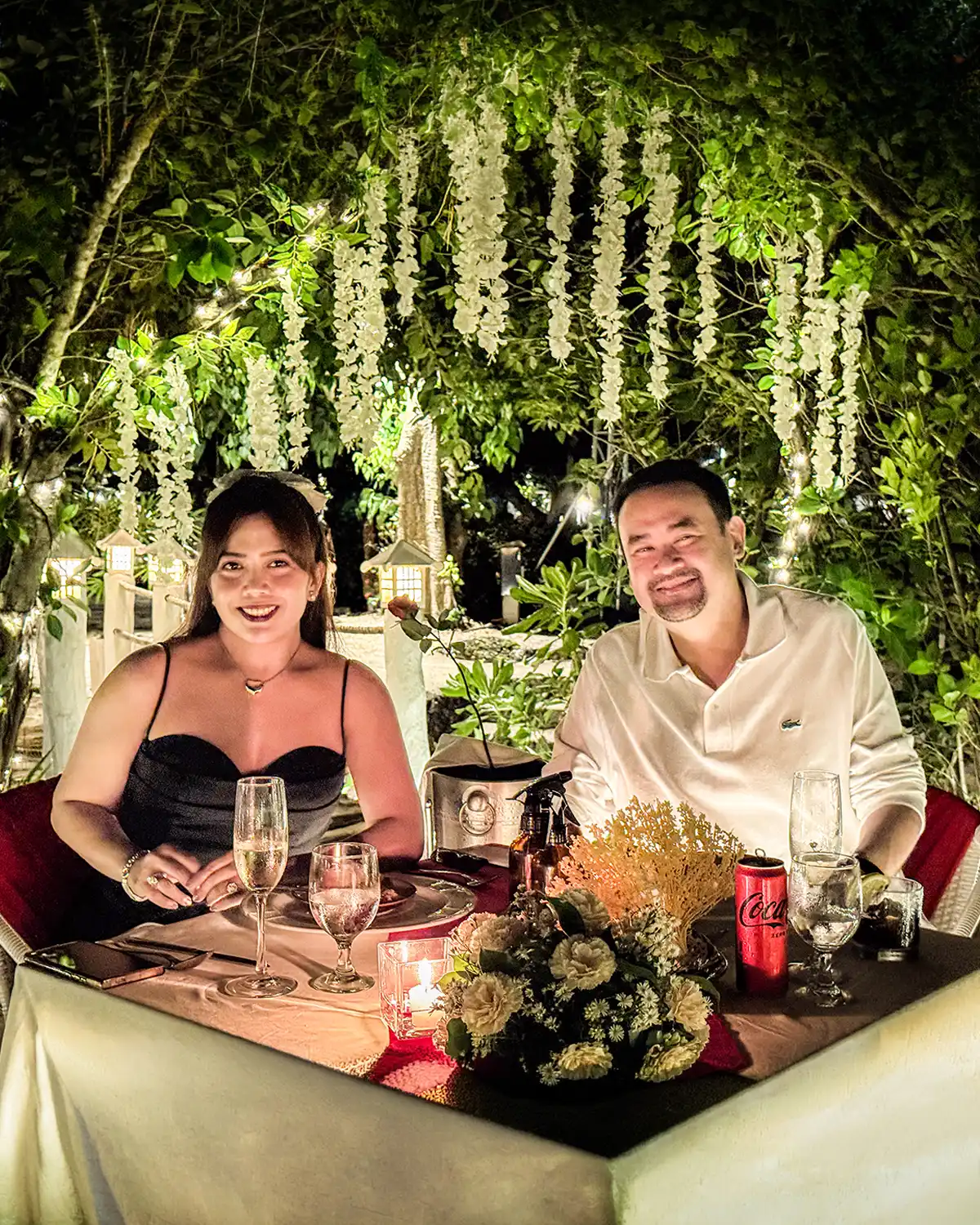 Couple at a candlelit dinner table at Lover's Rock, under trees strung with lights and hanging blossoms