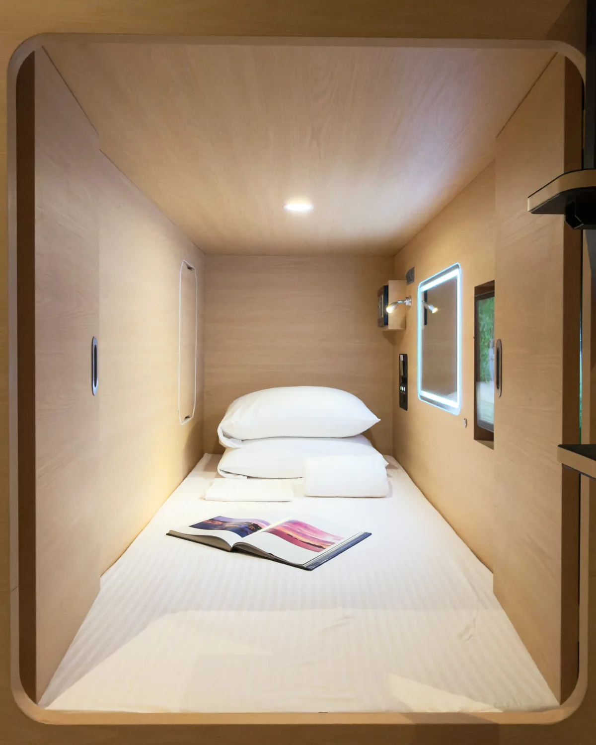 Inside an empty Youth Pod capsule: made-up bed, pillows and towels, lit vanity mirror and reading light