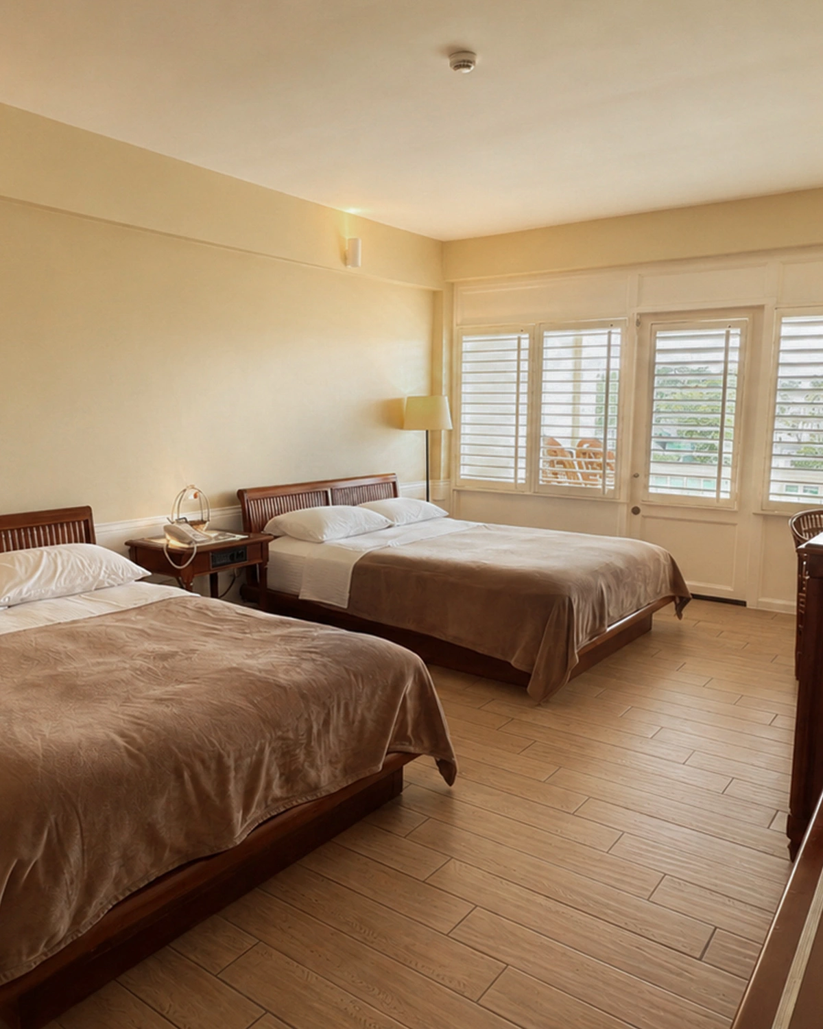 Two queen beds in a bright room with shuttered windows to the balcony