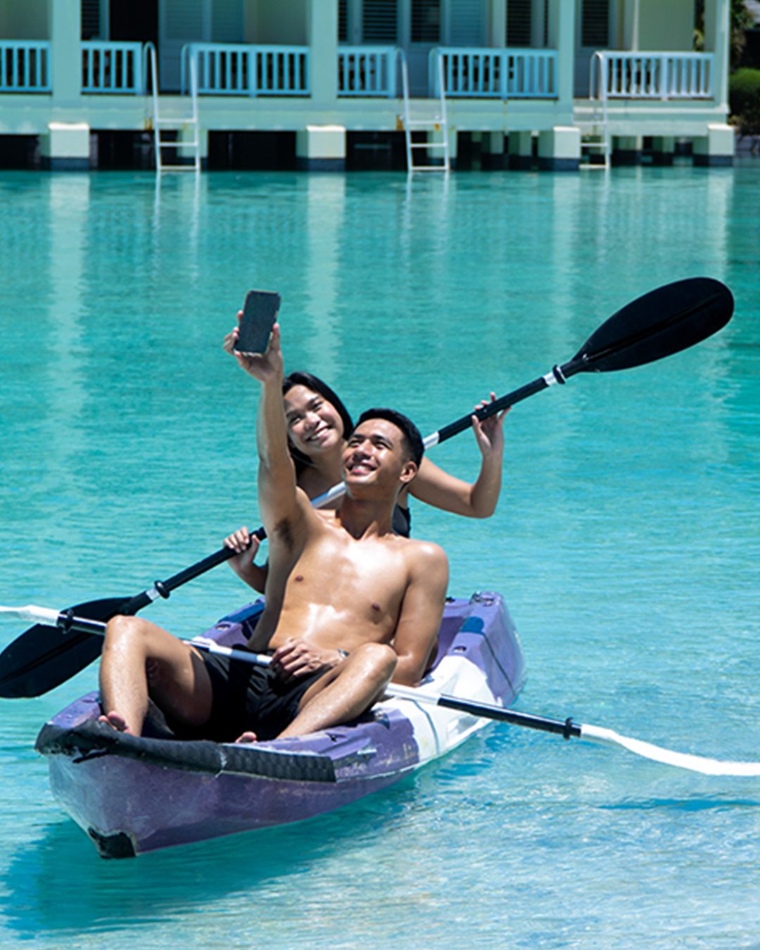A couple kayaking on Plantation Bay's saltwater lagoon, waterside rooms behind them
